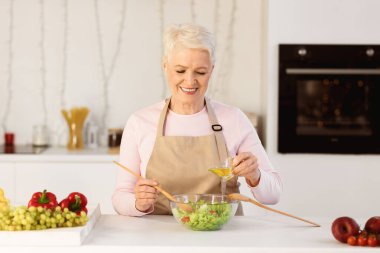 Gülümseyen yaşlı kadın modern mutfakta akşam yemeği için sebze salatası pişiriyor. İçeride Sağlıklı Yemek Hazırlayan Kıdemli Bayan. Yaşlılar için Beslenme ve Diyet Tarifleri