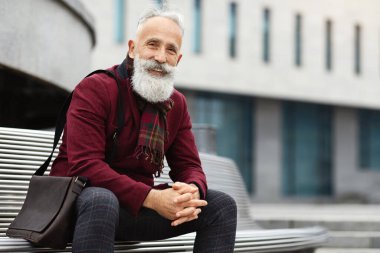 Yakışıklı, şık kıyafetli, şık sakallı adam bankta oturuyor, kameraya gülümsüyor, fotokopi çekiyor. Mutlu yaşlı işadamı boş zamanlarının tadını çıkarıyor, sokakta temiz hava soluyor.