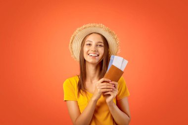 Yazlık şapkalı neşeli kız elinde pasaport ve uçuş biletleri, sarı stüdyo geçmişi.