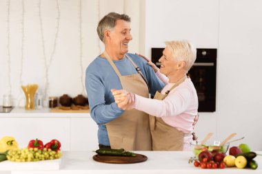 Neşeli Yaşlı Eşler Modern Mutfakta Dans Ediyor. Olgun bir çift hafta sonu birlikte yemek pişiriyor. Yaşlı aile eğlencesi, emekli yaşam tarzı ve mutluluk.