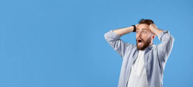 Şok olmuş milenyum adamı bağırıyor ve kafasını inançsızlıkla tutuyor, mavi stüdyo arka planındaki boş alana bakıyor, afiş tasarımı. Şaşkına dönmüş sakallı adam çığlık atıyor.