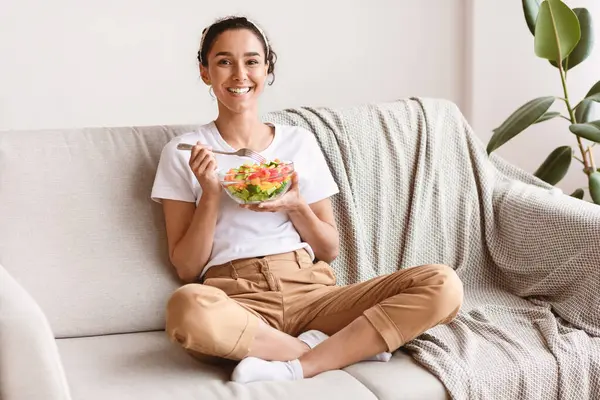 Oturma odasında rahat rahat oturup sebze salatası yiyen, fotokopi çeken güzel bir kadın. Mutlu güzel bayan sağlıklı bir hayat sürüyor, taze sebzeler yiyor, ev yapımı.