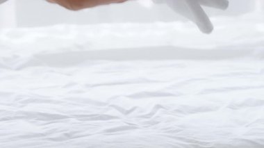 Genç bir kadın, yumuşak beyaz yatak örtüleriyle çevrili, rahat evinde dinleniyor. Huzurlu bir sabah atmosferine dalıp sükunetin özünü yakalıyor..