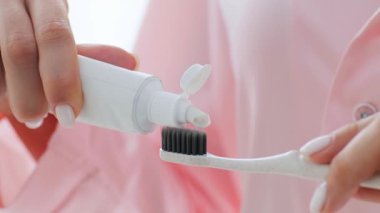 Genç bir kadın, diş fırçasına kişisel bakım ve güzellik odaklı diş macunu uygulayarak sabahları evdeki günü için hazırlanıyor. Sarı saçları ışıkta parlıyor..
