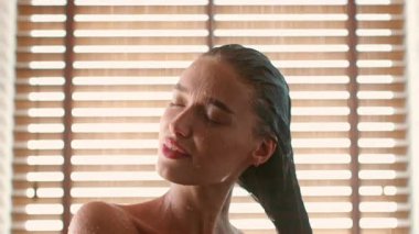 Bin yıllık bir kadın, narin bir duşun altında kendini şımartıyor, gözleri kapalı ve rahat, ahşap çatalların arasından süzülen sıcak ışıkla çevrili. Su cildinde parıldıyor, özgüvenini somutlaştırıyor..