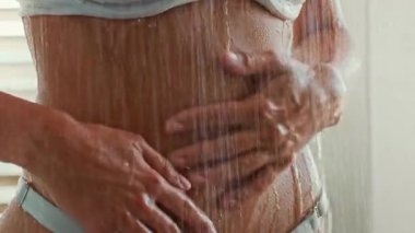 Duşta duran genç bir kadın, bir güzellik gösterisine girişirken vücudunun üzerinde çağlayarak akan su. Ellerini cildine özen ve besin sağlamak için kullanıyor. Kendini şımartma anını kucaklıyor..