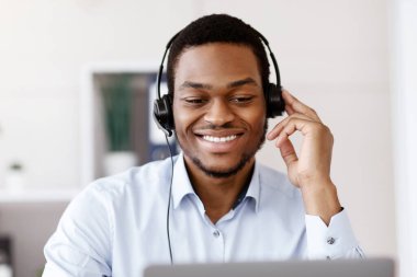 Kulaklıklı siyahi işçinin bilgisayarı kullanması, müşteriyle ya da iş ortağıyla neşeli bir şekilde konuşması bilgisayar ekranına gülümsemesi, Afro-Amerikan bir adamın iş eğitimi alması, kopyalama alanı.