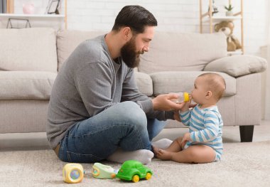 Katta evde oynarken küçük bebek oğlu su veren genç Baba