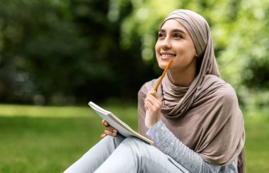 Başörtüsü içinde güzel bir kız kompozisyon yazıyor, halk parkında çalışıyor, boşluğu kopyalıyor.