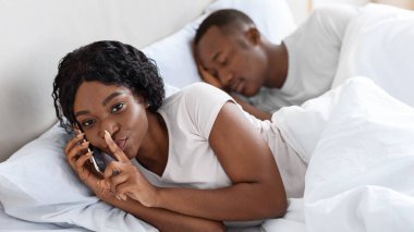 Siyahi bir kadın yatakta sevgilisiyle konuşurken kocası uyuyor, ilişki kavramında aldatıyor. Afrikalı Amerikalı kadın telefonda konuşurken kameraya şşş hareketi yapıyor.