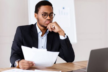 Gözlüklü, pazarlama raporlarını okuyan, ofisteki bilgisayarının önünde oturan Afrikalı Amerikalı işadamı evrak işleriyle uğraşıyor, maddi sorunları var, kopyalama alanı kullanıyor.