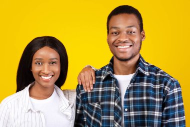 Aile fotoğrafı, birbirini seven ve birlikte eğlenen bir çift. Bin yıllık gülümseyen Afrikalı Amerikalı kadın elini kocalarının omzuna koydu ve sarı arka planda izole edilmiş boş bir yere baktı.