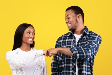 Takım olarak çalışın, bir şeyi kabul edin, gülümseyin ve olumlu olun. Komik Afro-Amerikan öğrenci erkek ve kadın gelişigüzel yumruk atıyor, sarı arka planda izole edilmiş, boş alan, stüdyo çekimi.