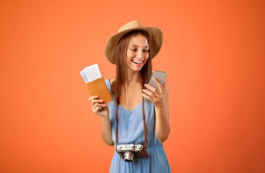 Turistler ve gezginler için mobil başvurular. Yazlık şapkalı mutlu kadın cep telefonu, pasaport ve uçuş biletleri tutuyor sosyal medyada paylaşıyor, sarı stüdyo geçmişi, kopyalama alanı