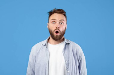 Afallamış genç adamın portresi mavi stüdyo arka planında şok içinde ağzını açıyor. Şok olmuş yüz ifadesini takınan sıradan giysili hayret verici bin yıllık adam, şansına inanamıyor, inanılmaz haberler öğreniyor.