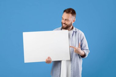 Pozitif genç adamın portresi boş reklam panolarına bakıyor ve senin tasarımın için bir maket yapıyor. Günlük giysiler içindeki neşeli sakallı adam boş afiş ya da fotokopi alanı olan poster gösteriyor.