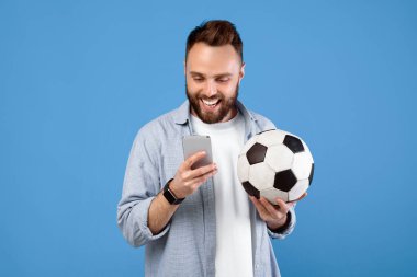 Futbol topu kullanan, akıllı telefon kullanan, spor bahsini kazanan, mavi stüdyoda en sevdiği takımı destekleyen genç adam. Milenyum adamı çevrimiçi futbol şampiyonasını izliyor