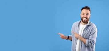 Heyecanlı genç sakallı adam gülümsüyor ve mavi stüdyo arka planındaki boşluğu işaret ediyor, panorama. Şaşırmış Kafkasyalı adam inanılmaz bir teklif alıyor, ürünü tanıtıyor.