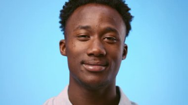 Genç bir Afrikalı Amerikalı, kameraya bakarken mutlu bir yüz ifadesi sergiliyor. Sade mavi arka plan, onun özelliklerini ve kendine güvenen tavırlarını vurguluyor.