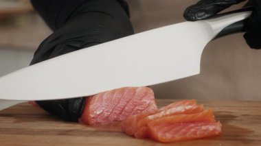 Siyah eldiven giyen yetenekli bir şef modern bir mutfakta tahta kesme tahtasında taze somon dilimler. Çevre, sağlıklı, çevre dostu aşçılık uygulamalarına bağlılığın altını çiziyor.