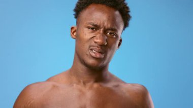 Genç bir Afrikalı Amerikalı kollarını esnetiyor, kaslarını gösteriyor. Kendine güvenen bir ifade sergiliyor, canlı mavi bir arkaplan ile sahneyi büyütüyor..