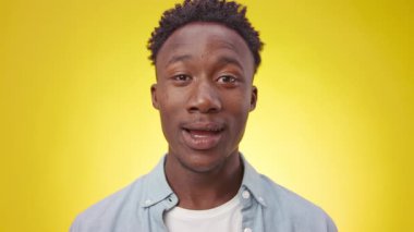 Genç bir Afrikalı Amerikalı, geniş bir gülümseme ve kollarıyla heyecan sergiliyor. Parlak sarı bir arka planın önünde duruyor, pozitif enerji ve coşku yayıyor..