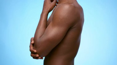 Dirseğine dokunan çıplak gövdeli genç bir Afro-Amerikan adam acı çekiyor. Açık mavi arkaplan