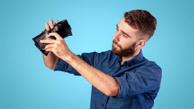 İflas, yoksulluk ve işsizlik. Zavallı genç adam mavi arka planda parasız boş cüzdana bakıyor. Ekonomik kriz sırasında maddi sorunları olan parasız bir milenyum adamı.