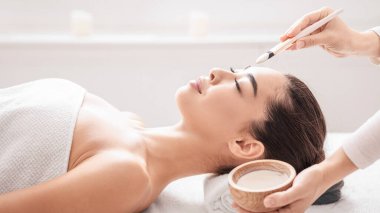 Profesyonel kozmetoloji. Spa Salonu 'nda güzellik uzmanı genç Asyalı kadına kilden maske takıyor, Kore' li rahat bir kadın sağlığın ve cilt bakımının keyfini çıkarıyor,