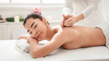 Profesyonel terapist, Spa salonundaki rahat Asyalı kadına sırt masajı yapıyor, güzel Koreli kadın, kapalı gözlerle masaya uzanıyor, vücut tedavilerinin ve sağlık prosedürlerinin tadını çıkarıyor,