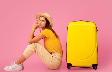 Bagajın yanında oturan üzgün kız, tatilin hayalini kuruyor, pembe stüdyo geçmişi.