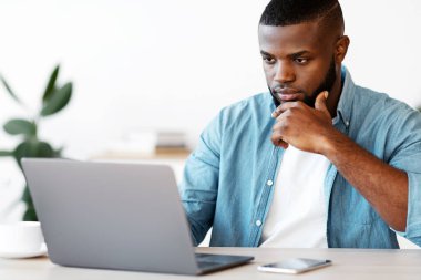 Ofiste dizüstü bilgisayarla çalışan, masada oturan, bilgisayar ekranına bakan, siyah girişimci, proje stratejisi ve iş planı hakkında düşünen,