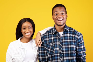 Mutlu insani duygular. Gülümseyen binlerce yıllık Afro-Amerikan çifti gündelik hayatta kameraya bakar, kadın elini erkeğin omzuna koyar, sarı arka planda izole edilmiş, stüdyo çekimi, kopyalama alanı.