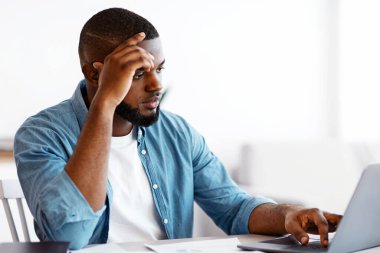 Çağdaş Girişimcilik. Genç Afro-Amerikalı iş adamı, İçişleri Bakanlığı 'nda dizüstü bilgisayarla çalışıyor, Millennial Black Man masasında oturuyor, bilgisayar ekranına bakıyor, uzaktan kumandalı bir işi, boş bir alanı var.
