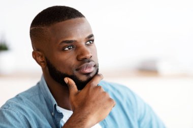 Çeneye dokunan ve başka tarafa bakan düşünceli siyah milenyum adamının portresi, dalgın sakallı Afrikalı Amerikalı bir adam bir şey düşünüyor, kafasının derinliklerinde oturuyor, fotokopi uzayı ile yakın plan çekilmiş.