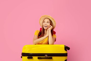 Pembe arka planda fotokopi alanına bakan heyecanlı kız çantanın yanında oturuyor.