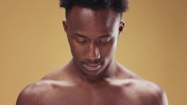 Genç bir Afrikalı Amerikalı adam sessizce dikiliyor, dalgın bir ifadeyle aşağıya bakıyor. Arka planda, samimi atmosferi arttıran yumuşak, sıcak bir renk var..