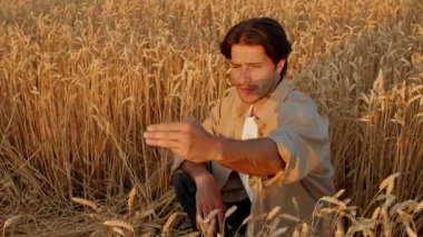 A young man in casual attire sits in a golden wheat field, gazing thoughtfully as the sun sets. The surrounding landscape is serene, bathed in warm light, creating a peaceful atmosphere.