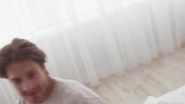 Beyaz çarşaflarla çevrili yumuşak bir yatakta yatarken bir çift birlikte güler. Güneş ışığı, neşeli gülüşleri ve samimi konuşmaları paylaşan sıcak ve davetkar bir atmosfer yaratır..