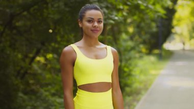 Genç bir Afrikalı Amerikalı kadın canlı sarı bir kıyafetle koşmaktan hoşlanıyor. Yeşillik ve güneş ışığı altında sağlıklı bir yaşam tarzını kucaklayarak yemyeşil bir parkta koşuyor..
