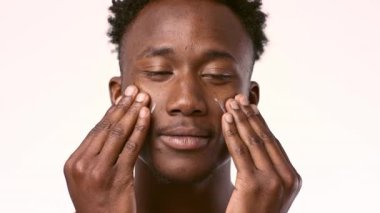 Beyaz, tarafsız bir arkaplana yüz kremi süren genç bir Afrikalı Amerikalı. Erkek konsepti için cilt bakımı