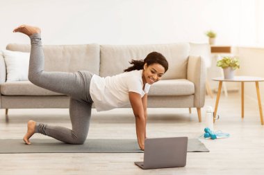 Çevrimiçi antrenman. Genç Afro-Amerikan Kadın Antrenman yapıyor dizüstü bilgisayar başında video izliyor, pilates yapıyor ya da yatak odasında yoga yapıyor ya da oturma odasında. Kadın Antrenman Karın kasları, Kaldırma Bacağı
