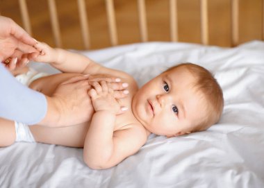 Tanımlanamayan anne, sevimli bebek vücuduna masaj yapıyor. Uyandıktan sonra anne eliyle oynarken kameraya bakan, tahta bebek yatağında uzanan sevimli çocuk.