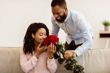 Beklenmedik bir sürpriz. Gülümseyen Afro-Amerikan bir adamın portresi mutlu bayanına bir demet kırmızı gül veriyor, güzel siyah kadın evdeki kanepede oturan çiçek buketini kokluyor. Kutlama