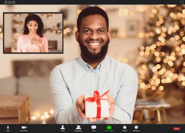 Karantina sırasında online parti. Gülümseyen Afro-Amerikan sakallı adam çevrimiçi video görüşmesi yapıyor, video kasette sürpriz mutlu kız arkadaşına hediye kutusunu gösteriyor. Konferans uygulaması ile ekran görüntüsü
