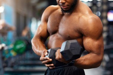 Pazı egzersizi. Konsantre Afro-Amerikan üstsüz sporcu spor salonunda dambıllarıyla kollarını eğitiyor, boş alan. Seksi siyah vücut geliştirici, tek eliyle halteri kaldırıyor.