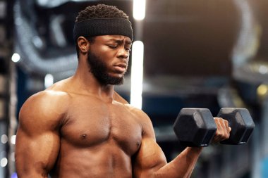 Konsantre ve yakışıklı Afro-Amerikan tişörtsüz vücut geliştirici spor salonunda koltuk değnekleriyle fotokopi odasına bakıyor. Ateşli siyahi adam iki dambılla egzersiz yapıyor, kasları üzerinde çalışıyor.