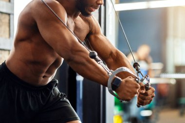 Genç siyahi sporcu trisepsleri spor salonunda, yan görüşte, fotokopi alanında çalıştırıyor. Gömleksiz Afrikalı Amerikalı vücut geliştirici modern spor salonunda çalışıyor, çapraz makine kullanıyor.