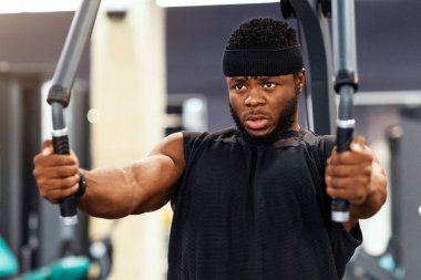 Spor salonunda omuz kaslarını ve göğüs kaslarını çalıştıran genç siyahi bir sporcu. Motive olmuş Afrikalı Amerikalı vücut geliştirici modern spor salonunda çalışıyor, Gaga güvertesi makinesi kullanıyor.