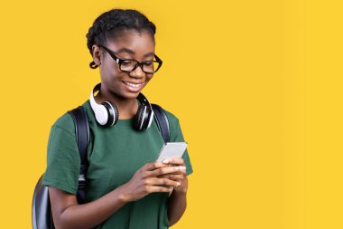 Akıllı Telefon Ağı Kullanan ve Çevrimiçi Mesajlaşan Mutlu Afrikalı Kız Öğrenci Sarı Arkaplanda Duruyor. Telefondaki cep telefonu uygulamasını kullanan genç kadın. Stüdyo Çekimi